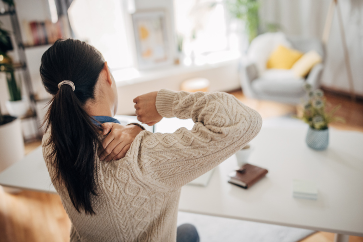 Een vrouw wrijft over haar pijnlijke schouder terwijl ze aan een bureau zit.