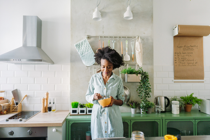 Een vrouw in een gestreepte ochtendjas staat in een moderne keuken en maakt haar ontbijt.