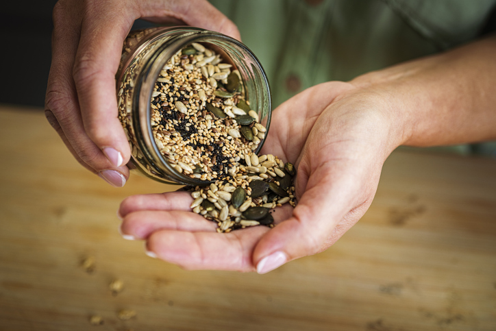 Vrouw strooit een mix van pitten en zaden vanuit een glazen pot op haar hand.