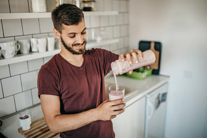 Een man in een keuken giet een eiwitshake in een glas.