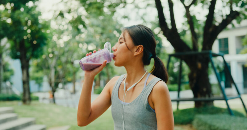 Een vrouw in sportkleding drinkt een eiwitshake.